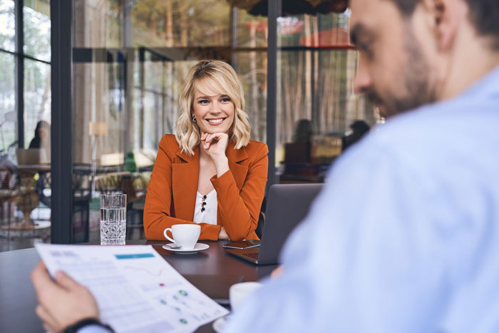 Female software developer in a client meeting looking surprised while a man reviews documents in a modern office. Female software developer in a client meeting looking surprised while a man reviews documents in a modern office.