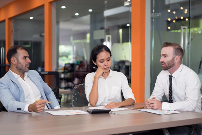 Female software developer looking thoughtful during a client meeting with two male colleagues in a modern office setting. Female software developer looking thoughtful during a client meeting with two male colleagues in a modern office setting.