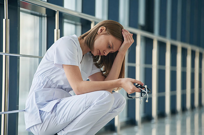 Woman in medical scrubs sitting on floor looking stressed, representing depressing weight and relationship issues. Woman in medical scrubs sitting on floor looking stressed, representing depressing weight and relationship issues.