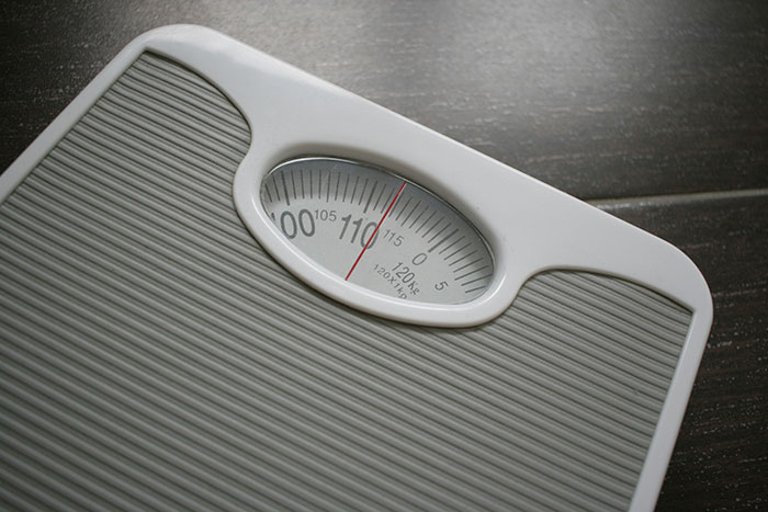 White analog bathroom scale showing a weight near 110 pounds on a dark wooden floor background. White analog bathroom scale showing a weight near 110 pounds on a dark wooden floor background.