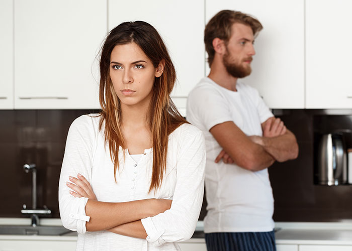 Woman called a gold digger standing with arms crossed while boyfriend looks upset in a modern kitchen.