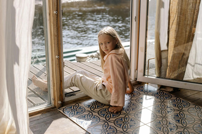 Young girl sitting by a doorway near water, looking thoughtful, capturing a moment in boyfriend daughter snitch drama. Young girl sitting by a doorway near water, looking thoughtful, capturing a moment in boyfriend daughter snitch drama.