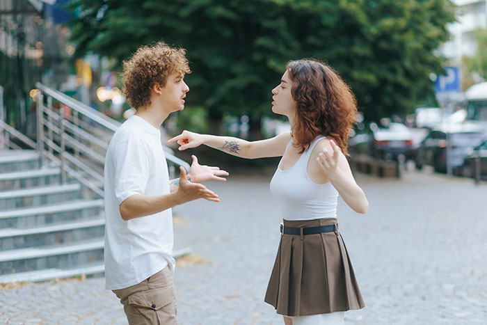 Man and woman arguing outdoors, tense confrontation showing conflict after discovering she secretly went clubbing.