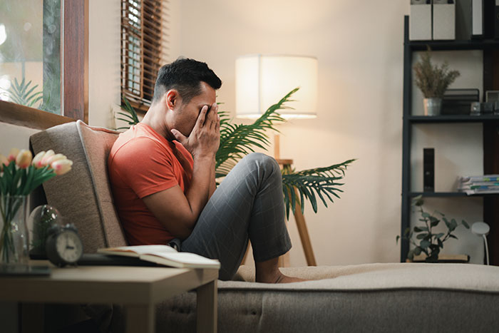 Man upset and stressed on sofa after discovering girlfriend secretly went clubbing and lost his car at home.