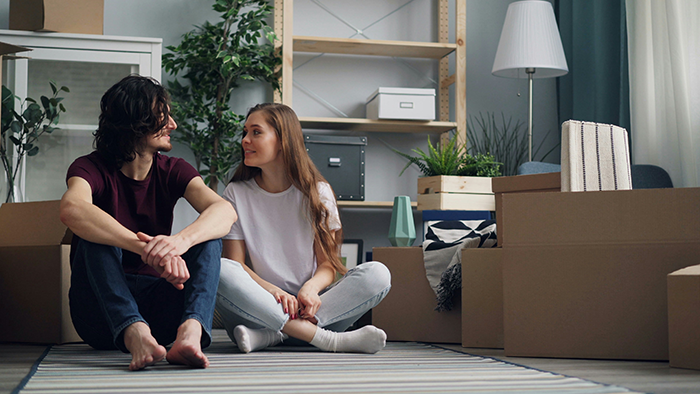 Young couple sitting on the floor among moving boxes, discussing a $100k renovation and relationship finances.