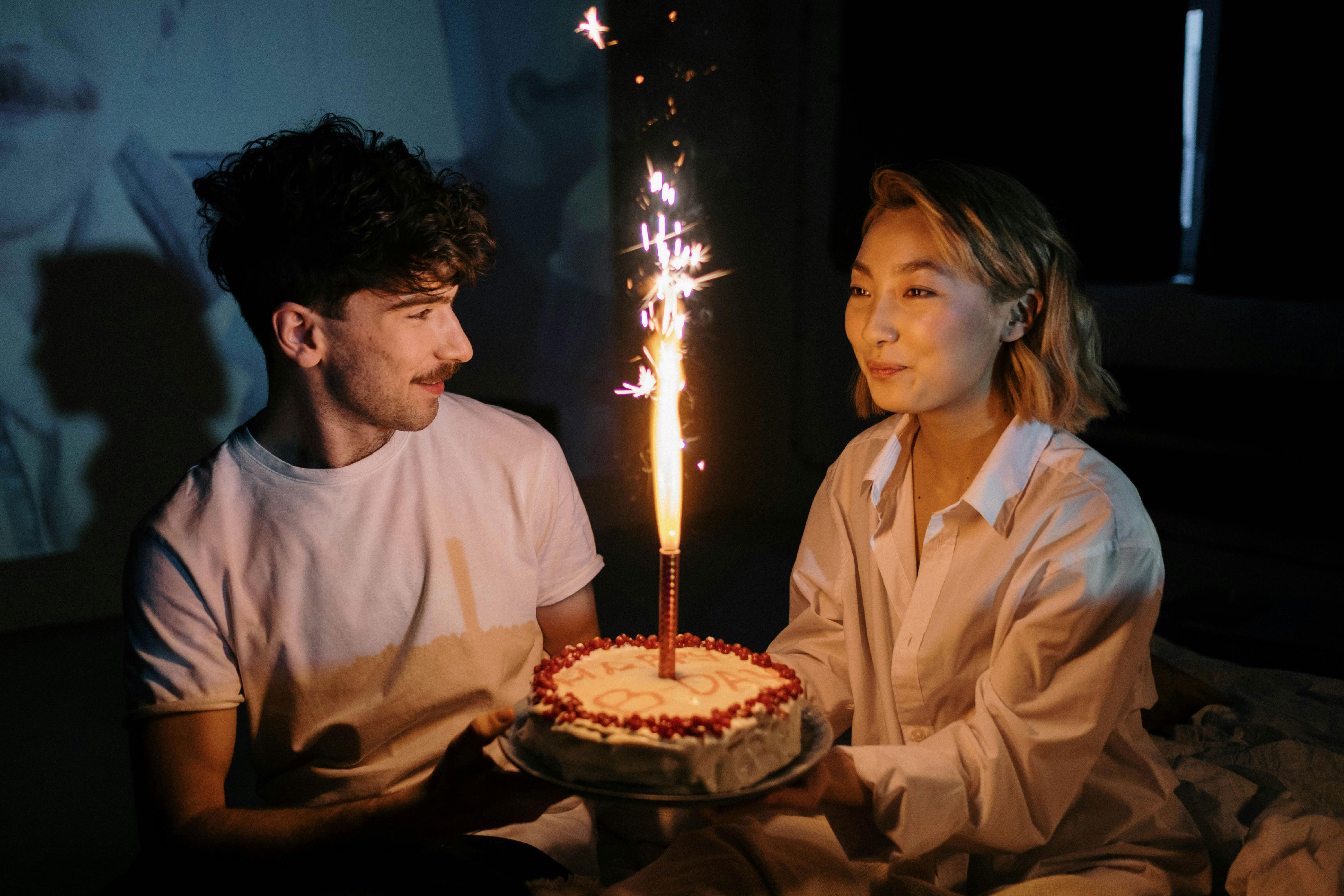 Couple holding birthday cake with sparkler candle, highlighting guy forgetting girlfriend's upcoming birthday.
