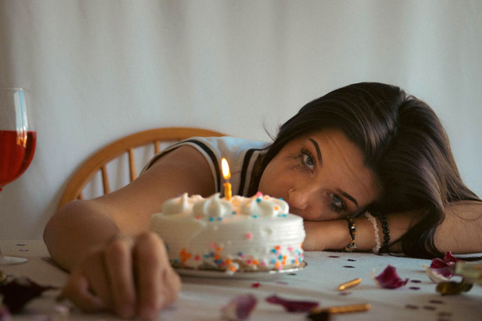 Woman looking sad with makeup smudged at birthday cake with one candle, highlighting forgotten birthday frustration.