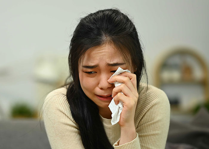 Woman crying and wiping tears, upset about leaving the US to start a new life in France after relationship struggles.