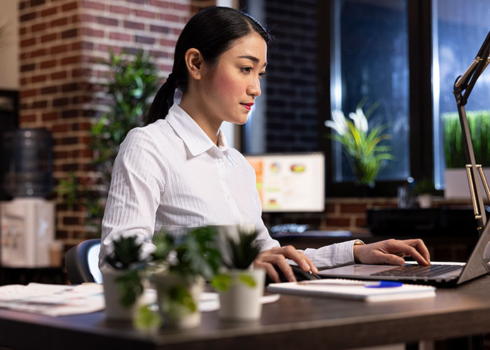 Woman working focused on laptop in modern office, starting new life abroad after success challenges in US.