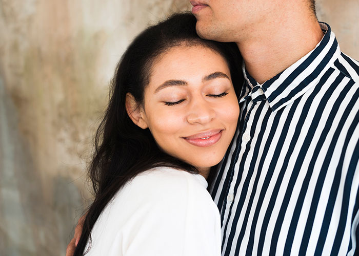 Woman smiling with eyes closed while hugging man in striped shirt, symbolizing woman success and new life in France.