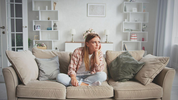 Young woman feeling uneasy sitting on sofa, worried about boyfriend mentioning moving in together at home. Young woman feeling uneasy sitting on sofa, worried about boyfriend mentioning moving in together at home.