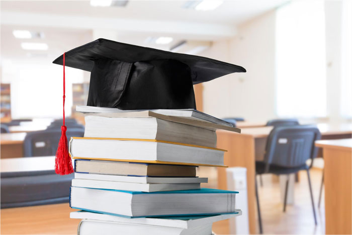 Graduation cap placed on a stack of books in a bright, empty university classroom symbolizing education and university life. Graduation cap placed on a stack of books in a bright, empty university classroom symbolizing education and university life.