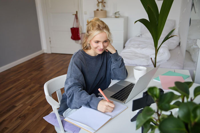 Young woman studying at home with laptop and notebook, hesitant about boyfriend opposing her university plans over trust issues. Young woman studying at home with laptop and notebook, hesitant about boyfriend opposing her university plans over trust issues.