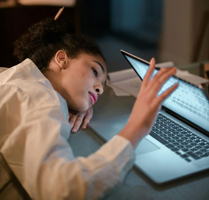 Young woman resting her head on a desk, looking at a laptop screen, reflecting on a guy refusing to accept break-up after a trip. Young woman resting her head on a desk, looking at a laptop screen, reflecting on a guy refusing to accept break-up after a trip.