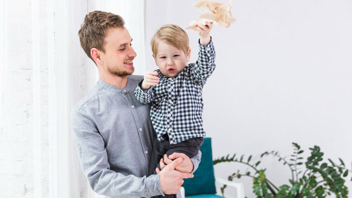 Man holding toddler playing with wooden airplane, representing woman moves in with boyfriend realizing he wanted nanny with benefits.