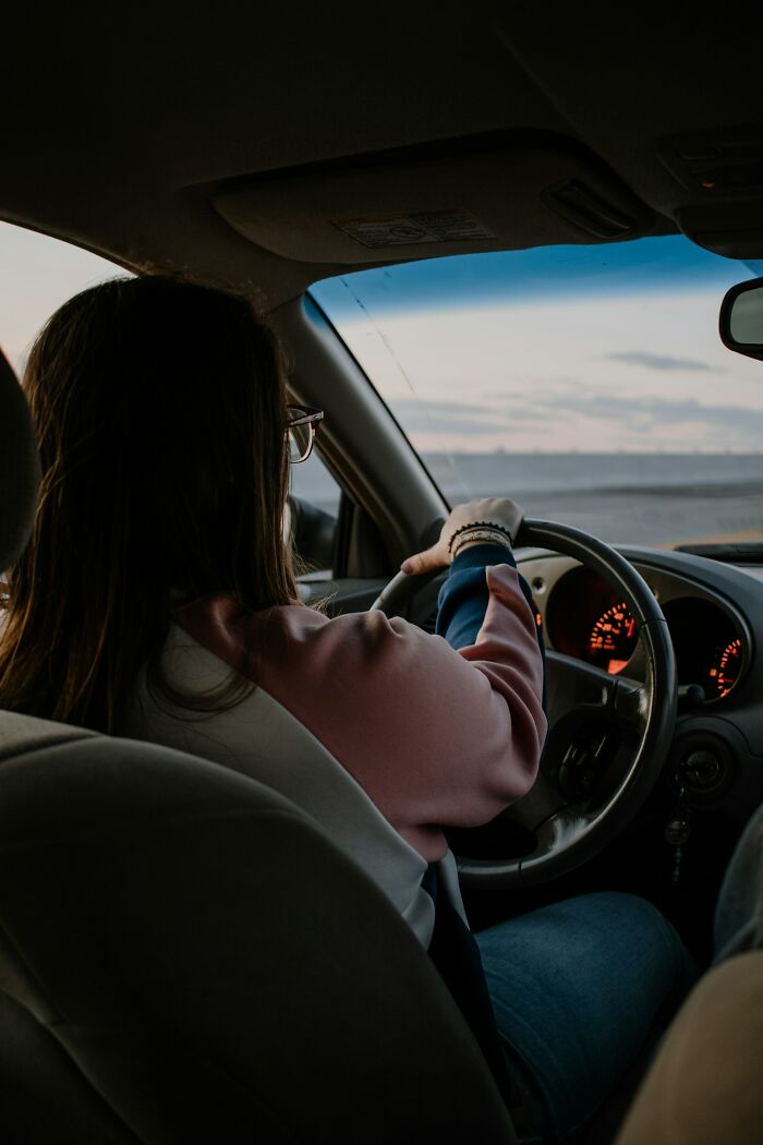 Person driving a car at dusk with a focus on the steering wheel and dashboard, symbolizing heavy confessions.