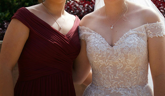 Bride in lace wedding dress standing next to cousin in a dark red dress, outdoors with natural light.