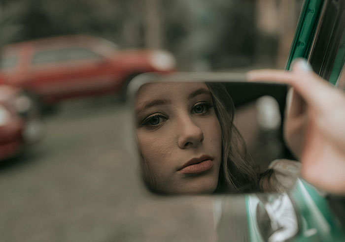 Close-up of a woman&rsquo;s face reflected in a car mirror, capturing a bride mad at cousin over dress at wedding.