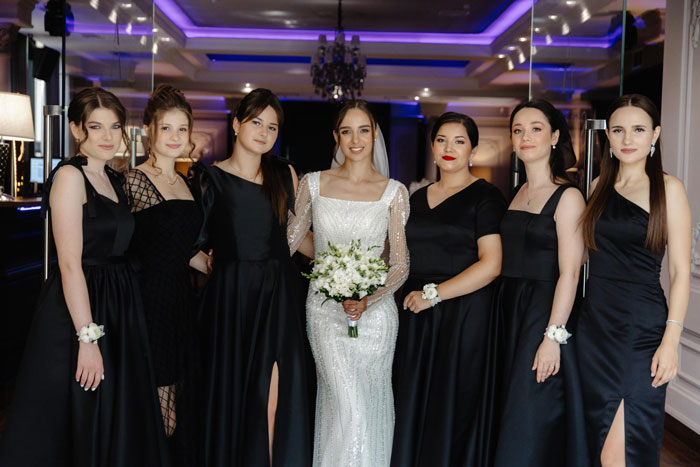Bride in white dress with bridesmaids wearing all-black dresses at wedding, except one bold red dress breaking the dress code.