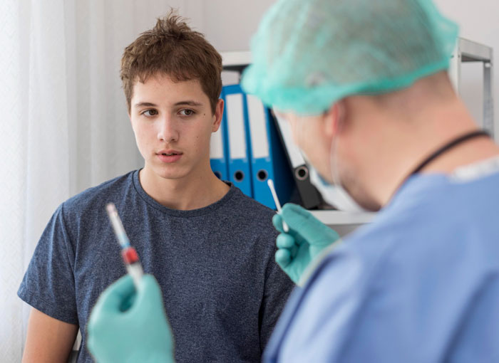 Teen boy in a medical exam room looking at doctor preparing a syringe, representing diabetes and weight health concerns.
