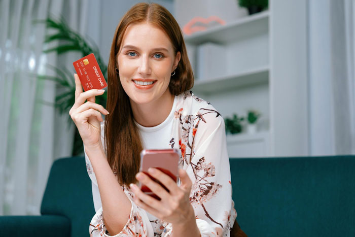 Young woman holding a credit card and smartphone, illustrating brother uses sister&rsquo;s credit card without permission issue.
