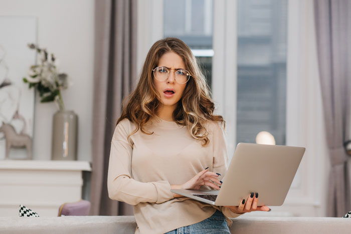 Young woman at home with a laptop looking shocked while dealing with unauthorized credit card use by brother.