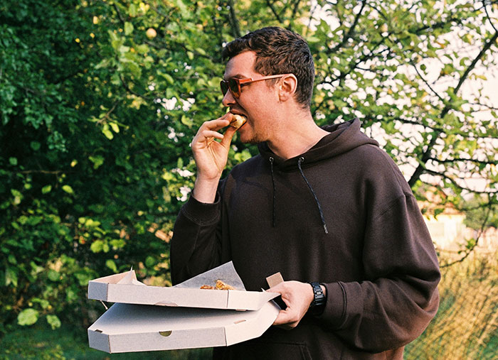 Man in sunglasses and hoodie eating pizza outdoors, enjoying a moment that shows how a bad day turned life-changing.