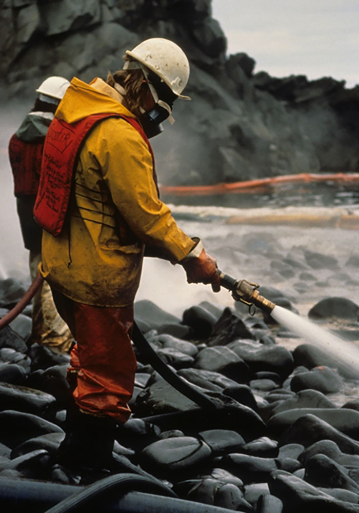 Worker in protective gear cleaning oil spill on rocky shore demonstrating business mistakes that lost clients.