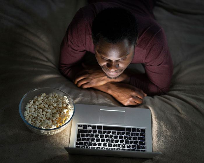 Man lying on bed watching laptop with a bowl of popcorn, representing businesses that lost clients with bad decisions.