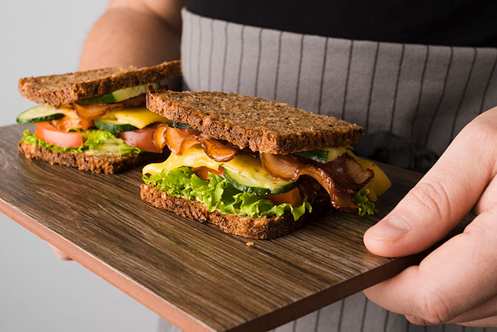 Two bacon and cheese sandwiches on whole grain bread held on a wooden board, illustrating businesses that lost clients.