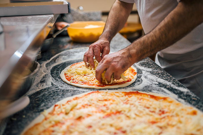 Hands of a pizza chef adding cheese on dough, illustrating businesses that lost their clients with bad decisions.