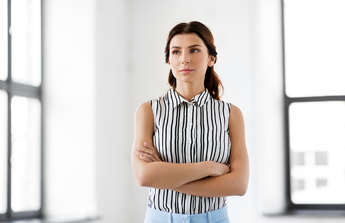 Young woman with arms crossed looking thoughtful in a bright room, reflecting on neglecting siblings and wanting to reconnect.