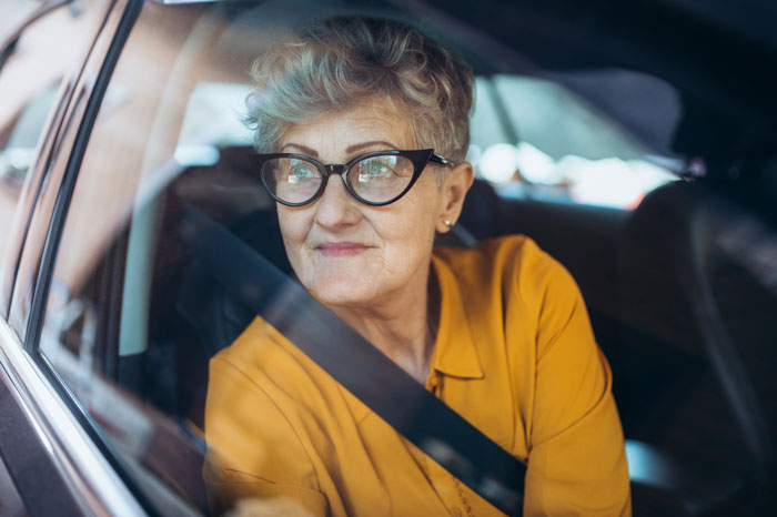 Elderly woman wearing glasses inside a car, seen through the window, suggesting a parking lot incident with a shopping cart.