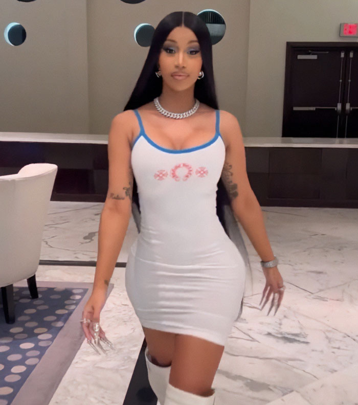 Woman in a fitted white dress and long black hair poses indoors, highlighting trends in plastic surgery regrets in 2025.