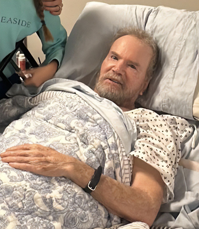 Elderly gravely ill veteran lying in hospital bed, covered with blanket, receiving care from a person nearby. Elderly gravely ill veteran lying in hospital bed, covered with blanket, receiving care from a person nearby.