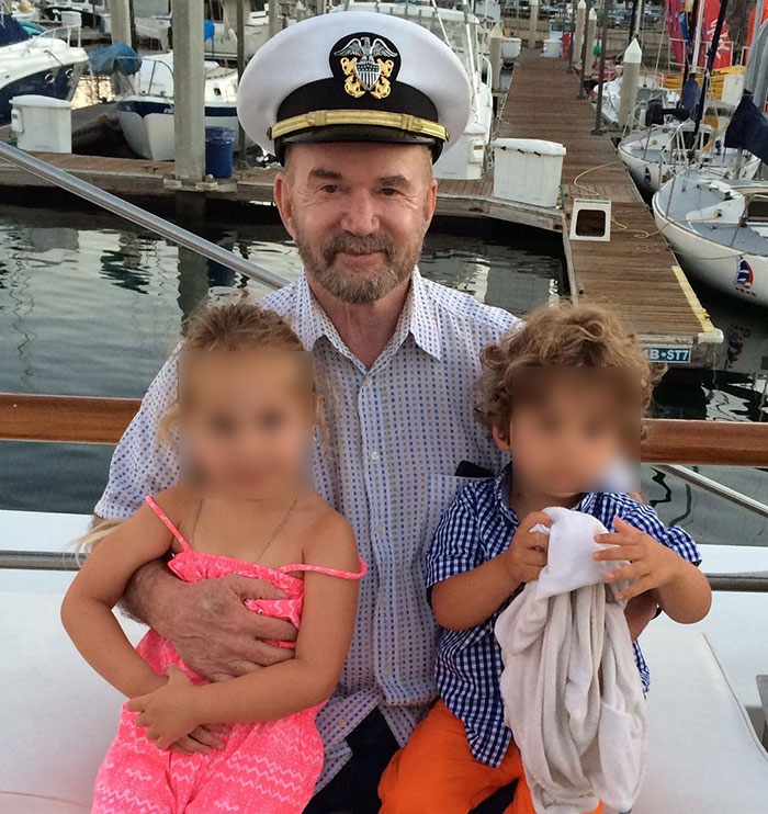 Elderly veteran in a naval officer hat smiling and holding two young children on a boat docked at a marina. Elderly veteran in a naval officer hat smiling and holding two young children on a boat docked at a marina.