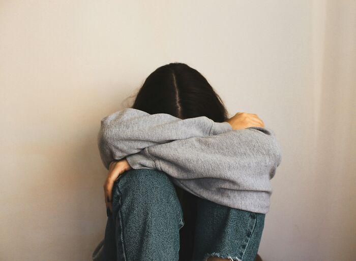 Person hiding face in arms sitting against wall, representing toxic relationship traits and emotional distress.