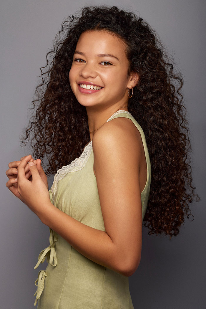 Young woman with curly hair smiling in a sleeveless green dress, linked to Disney live-action Moana star appearance controversy.