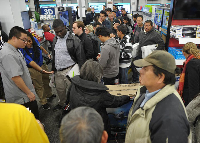 Shoppers crowded inside an electronics store during a chaotic sale event, with many holding products and waiting in line.