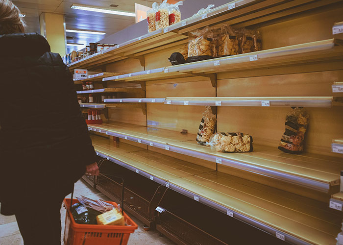 Person with shopping basket in front of empty grocery shelves, illustrating chaotic scenes witnessed in stores.