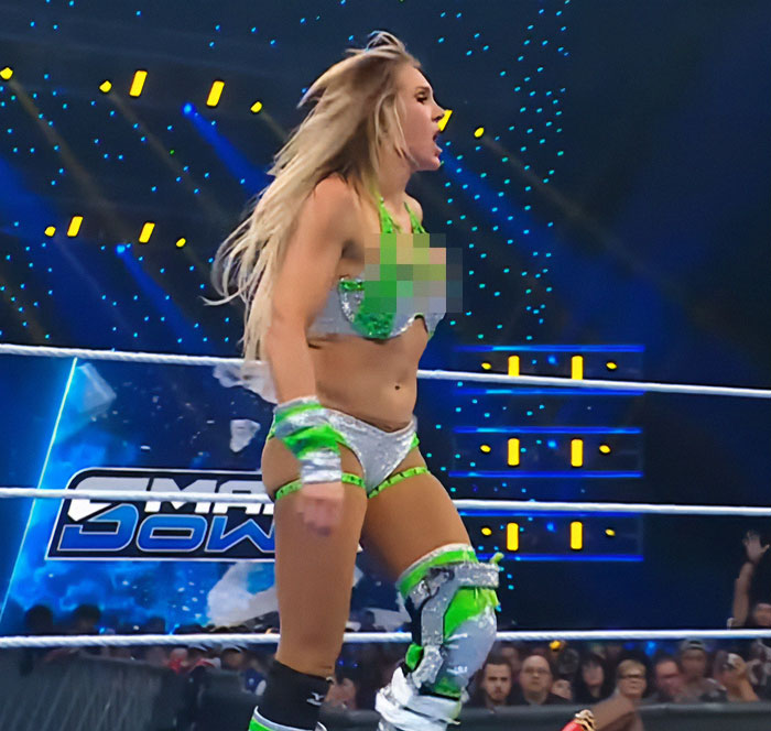 Female wrestler in green and silver outfit performing in a ring with an audience, celebrity revealed moments sparking a frenzy.