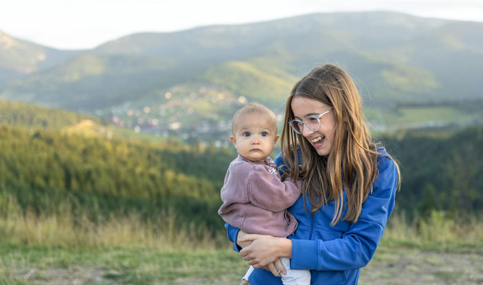 Teen sister holding baby outdoors in countryside, highlighting irresponsibility and parental challenges faced by teens. Teen sister holding baby outdoors in countryside, highlighting irresponsibility and parental challenges faced by teens.