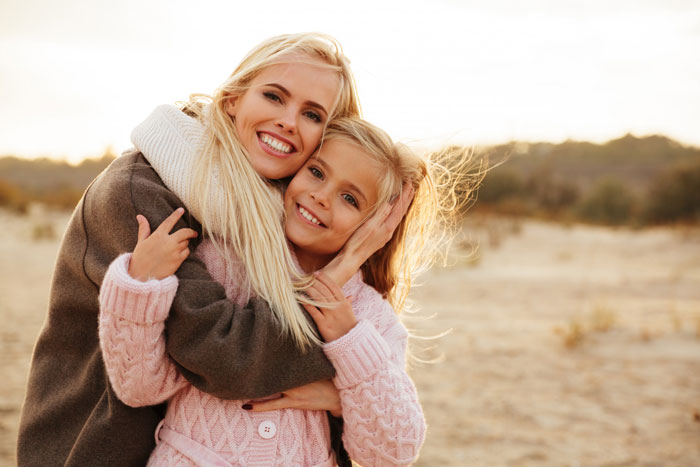 Mother and daughter smiling and hugging outdoors, highlighting the significance of mom&rsquo;s native language despite dad&rsquo;s ban.