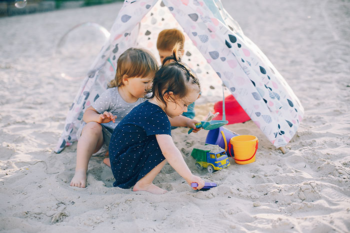 Three children playing with sand toys under a small tent, illustrating family and childfree cousin vacation conflict.