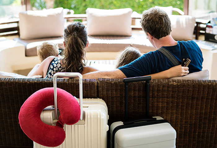 Family on vacation sitting on a couch with luggage nearby, highlighting a childfree cousin dynamic during the trip.