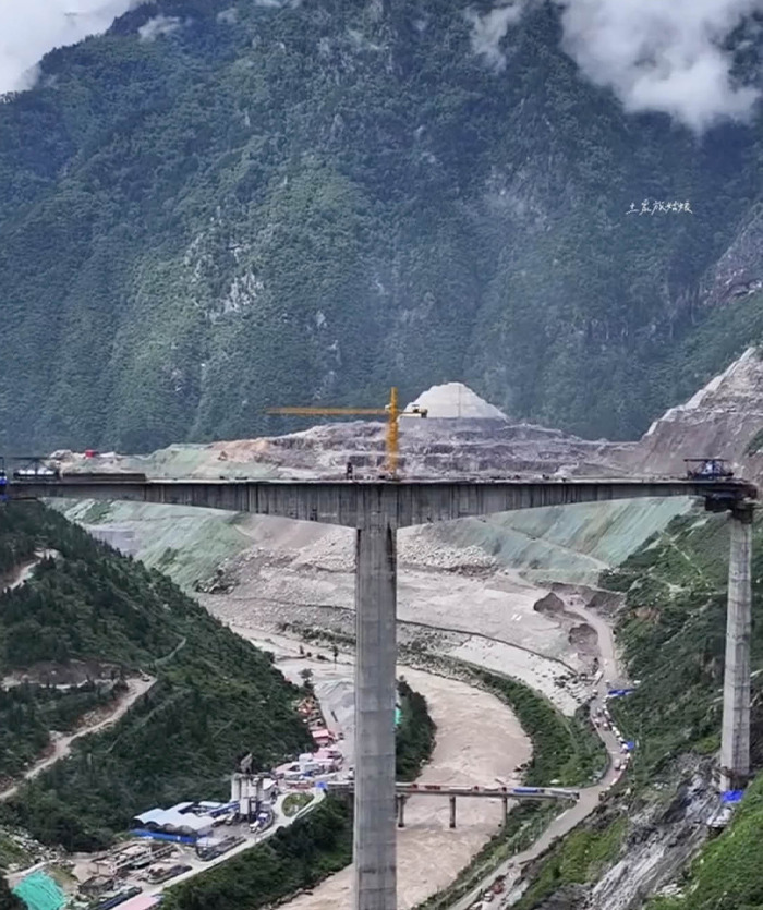 Partially built ambitious bridge in China spanning a deep valley with construction equipment and mountainous backdrop. Partially built ambitious bridge in China spanning a deep valley with construction equipment and mountainous backdrop.