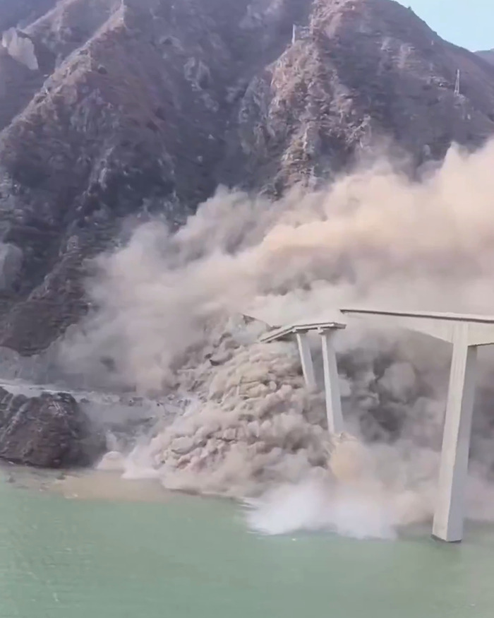 Bridge collapsing into dust with large cloud of debris near mountainous area and body of water in China. Bridge collapsing into dust with large cloud of debris near mountainous area and body of water in China.