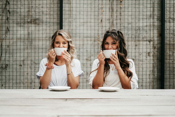 Two women sitting at a table drinking coffee, illustrating families where the golden child wasn't always golden.