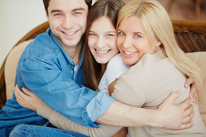 Family of three hugging and smiling, representing a man feeling like a single parent as wife prioritizes work over family.