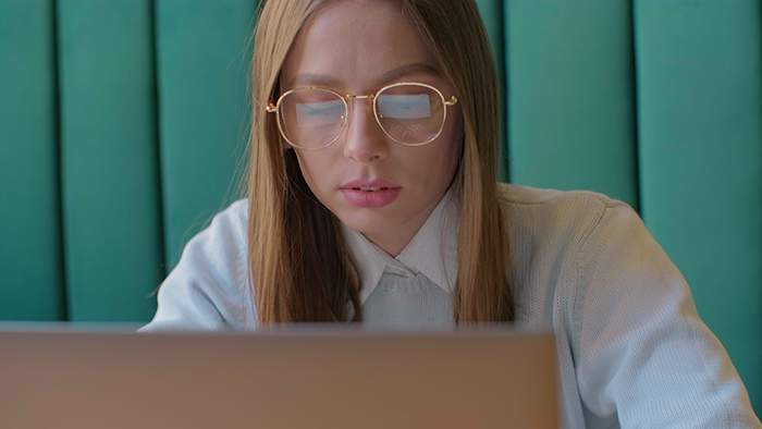 Woman with glasses looking at laptop screen, focused and concerned, exposing cheaters in an online investigation.